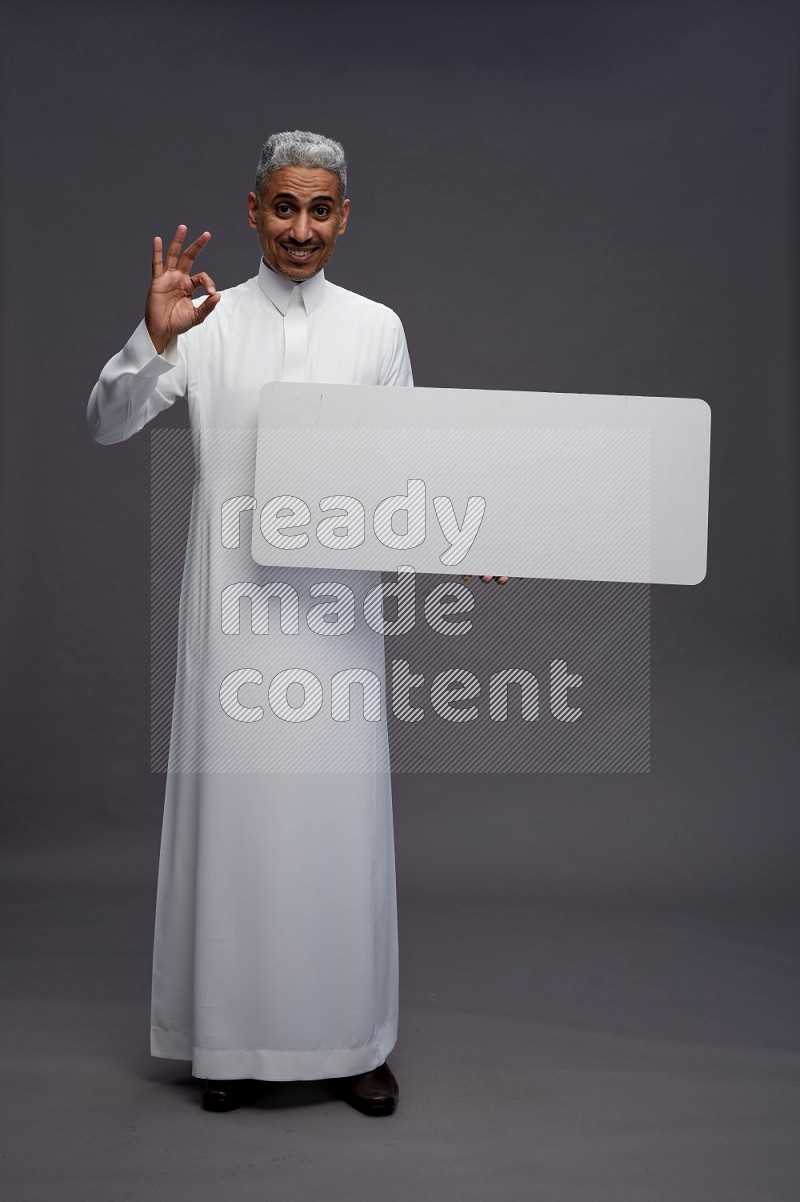 Saudi man wearing thob standing holding board on gray background