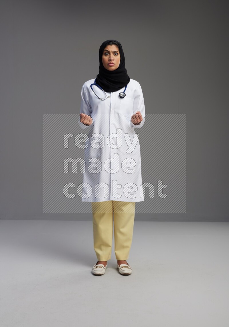 Saudi woman wearing lab coat with stethoscope standing interacting with the camera on Gray background