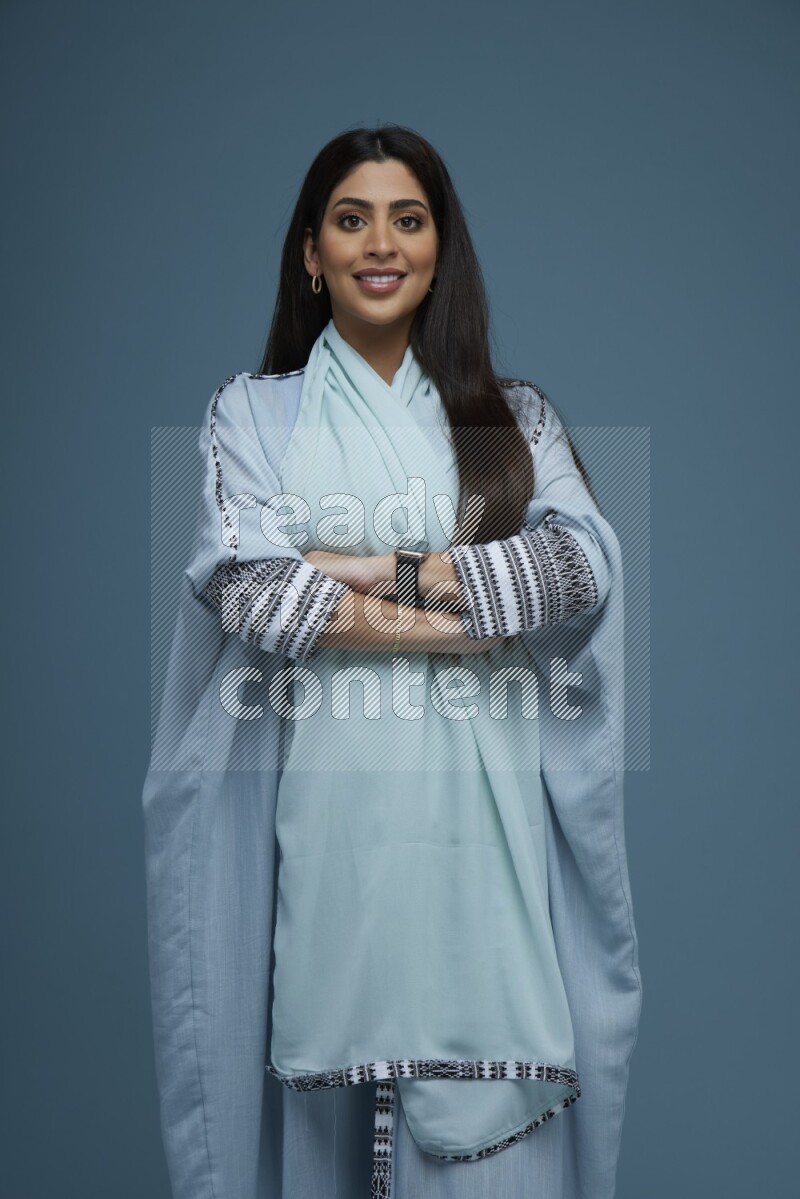 A woman posing in a blue background wearing blue Abaya no Hijab