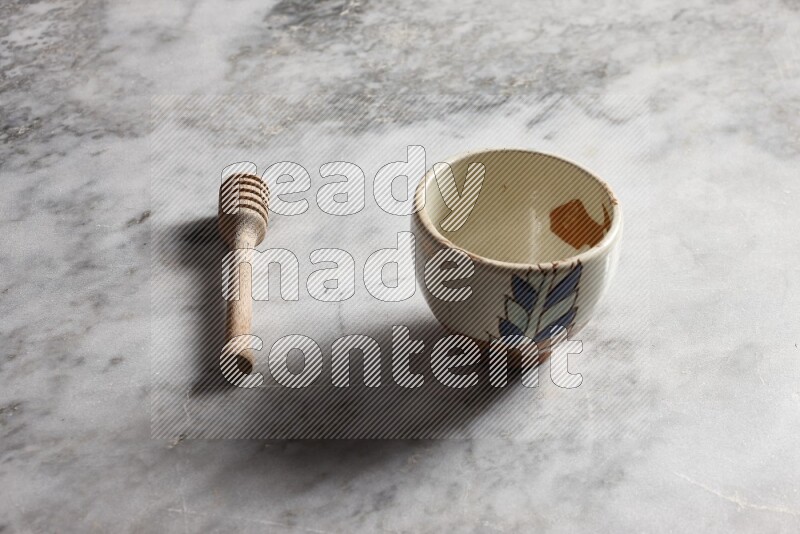 Decorative pottery bowl with wooden honey dipper on the side on grey marble background