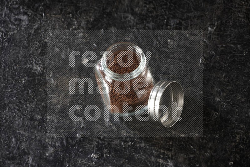 A glass spice jar full of cloves powder on textured black flooring