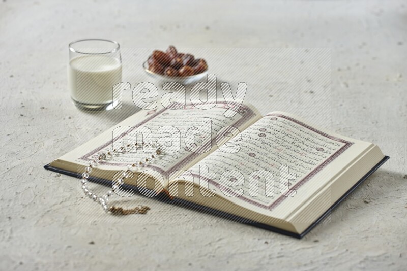 Quran with dates, prayer beads and different drinks all placed on textured white background