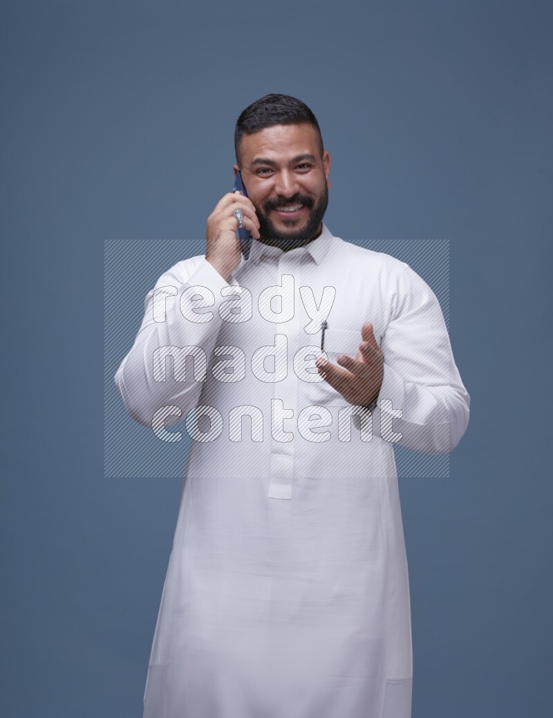 A Saudi man calling on blue background wearing Saudi Thob