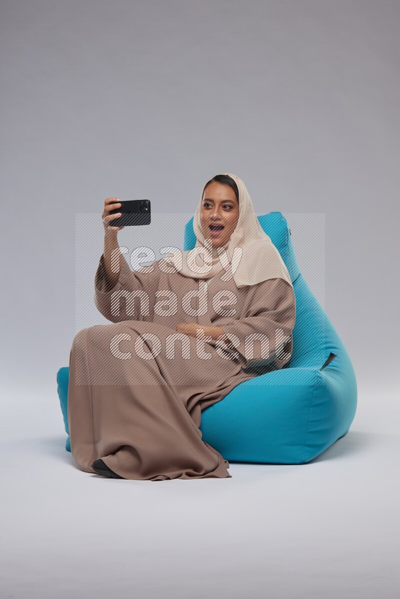 A Saudi woman sitting on a blue beanbag and taking selfie