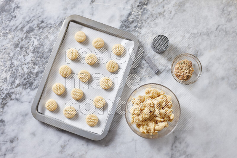 كحك خطوة بخطوة بمكوناته سمن، سكر، دقيق، سمسم، خميرة، ماء ونكهة الكحك على خلفية رخام رمادي