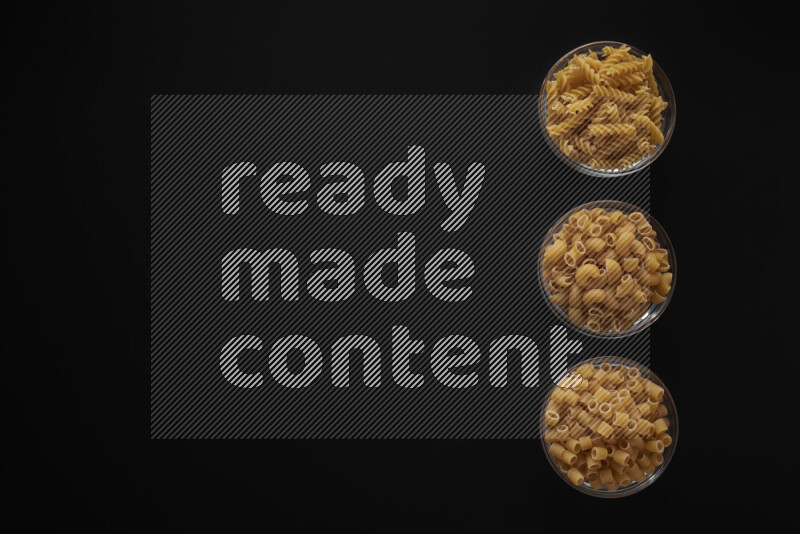 Different pasta types in 3 glass bowls on black background