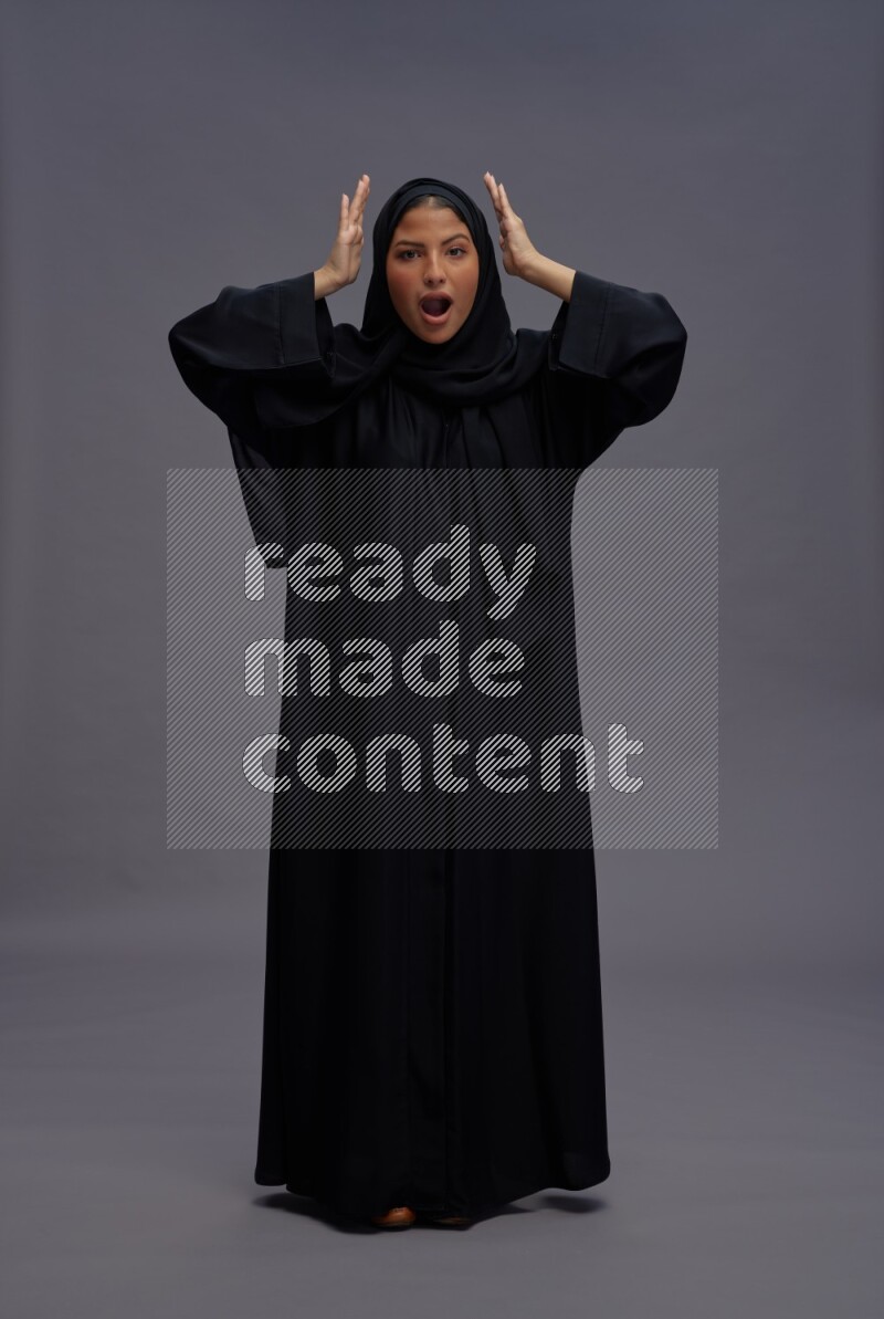 Saudi woman wearing Abaya standing hands behind head on gray background