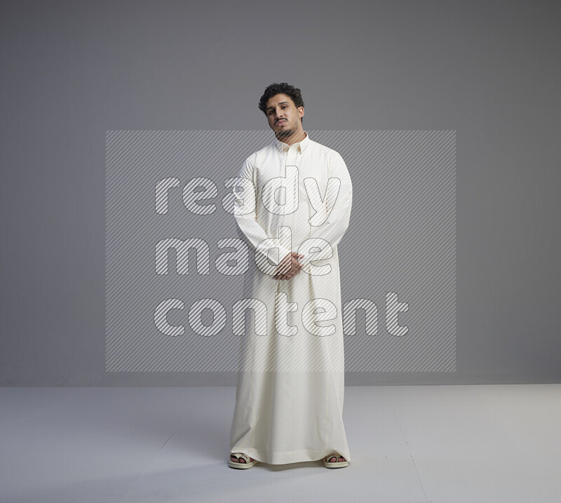 A Saudi man standing wearing thob interacting with the camera on gray background