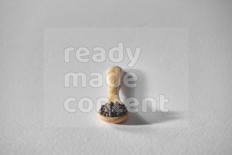 A wooden spoon full of black pepper on white flooring