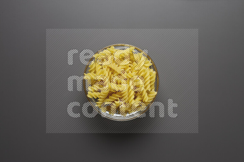 Fusilli pasta in a glass bowl on grey background