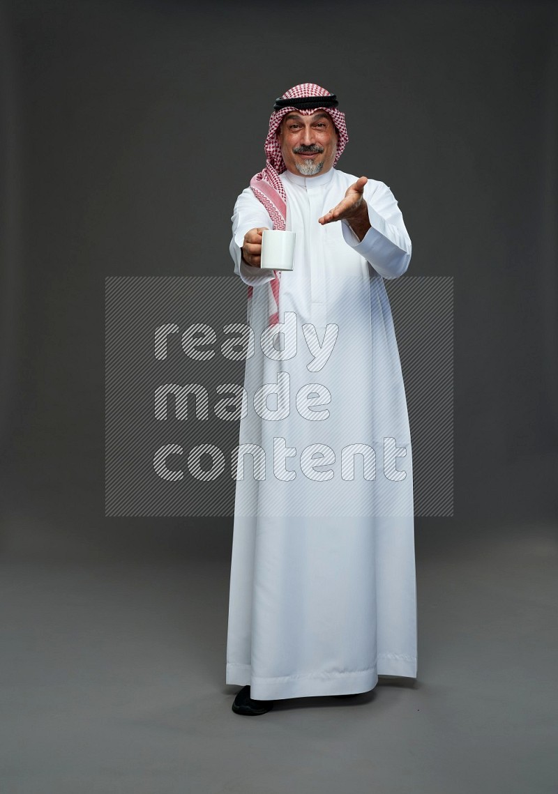 Saudi man with shomag Standing holding mug on gray background