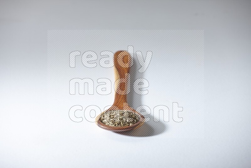 A wooden ladle full of cumin seeds on a white flooring