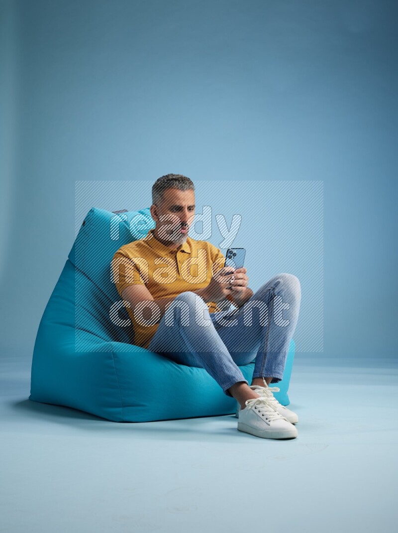 A man sitting on a blue beanbag and texting on phone