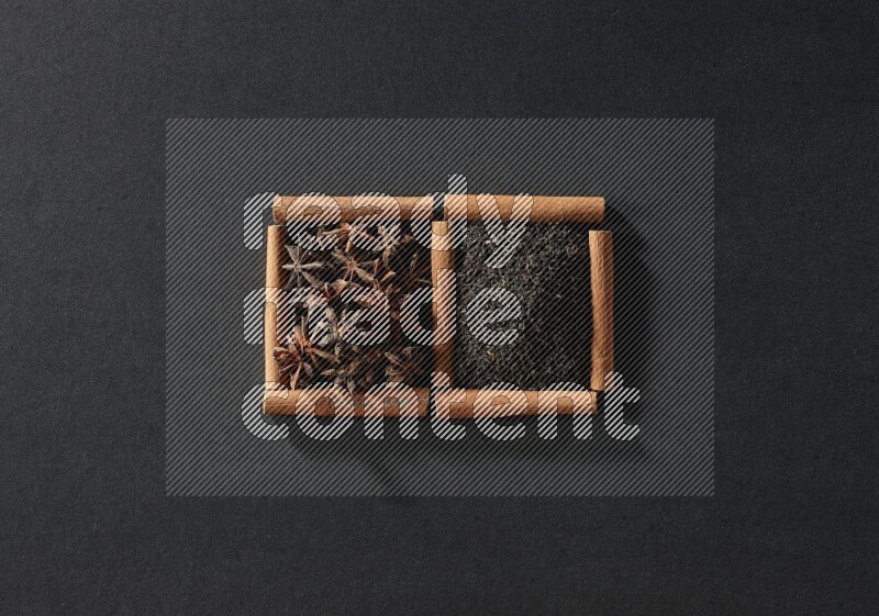 مربعان من أعواد القرفة ممتلئان باليانسون النجمي والشاي الأسود علي خلفية سوداء