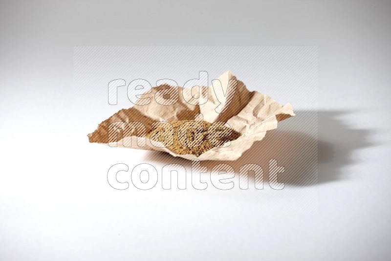 Cumin powder in a crumpled piece of paper on white flooring