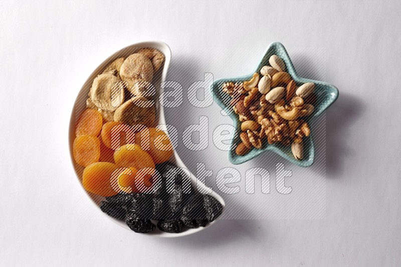 Mixed Dried fruits in a crescent pottery plate and a star shaped plate with mixed nuts on white background