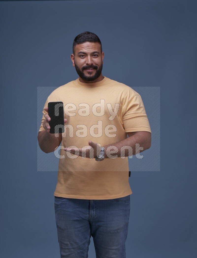 رجل يرتدي بنطال ازرق جينز وقميص اصفر بأكمام قصيره يشير الى جواله