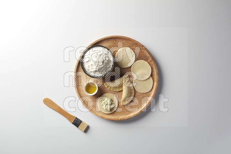 two closed sambosas and one open sambosa filled with cheese while flour, and oil with oil brush aside in a wooden dish on a white background