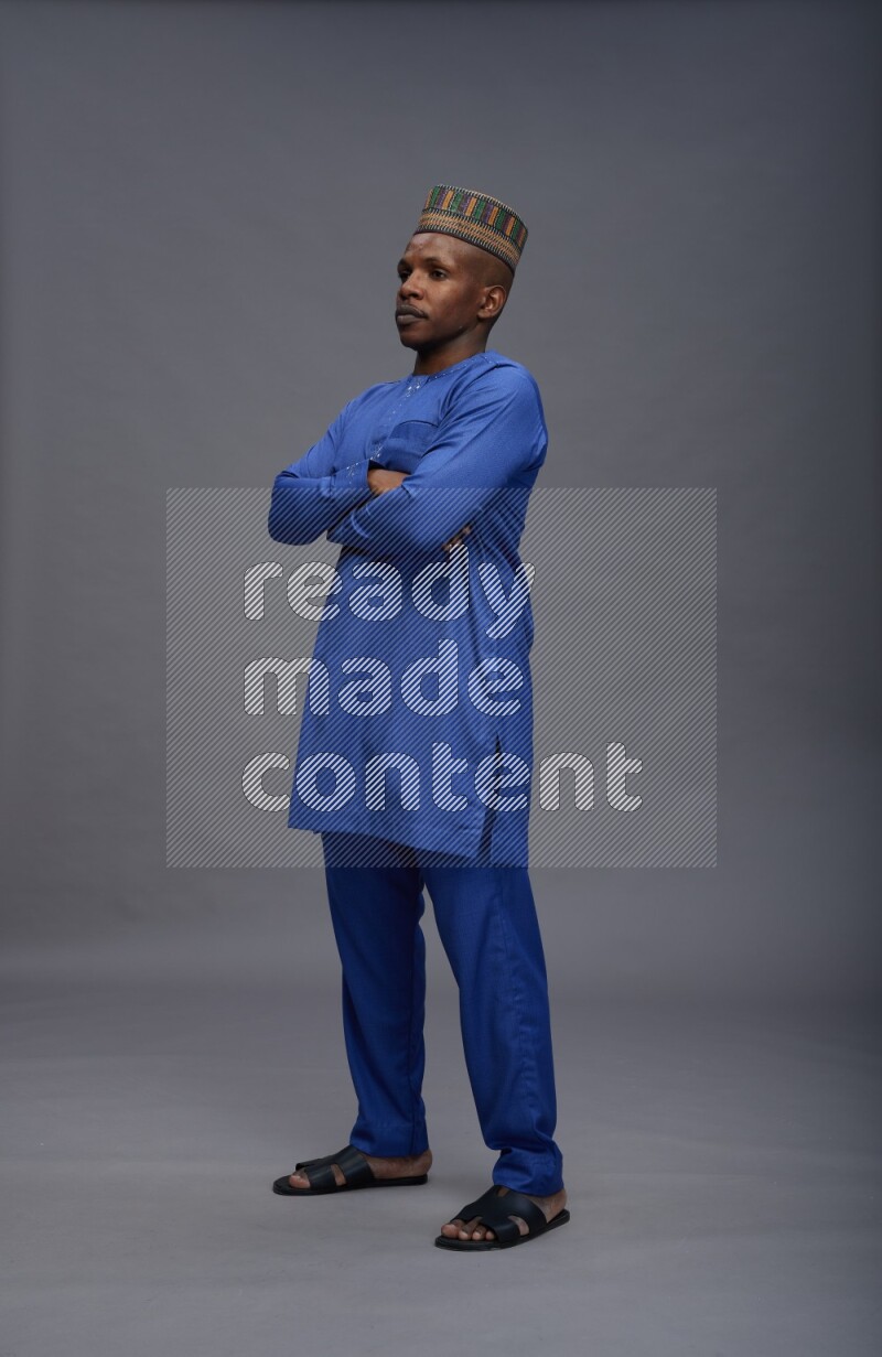 Man wearing Nigerian outfit standing with crossed arms on gray background