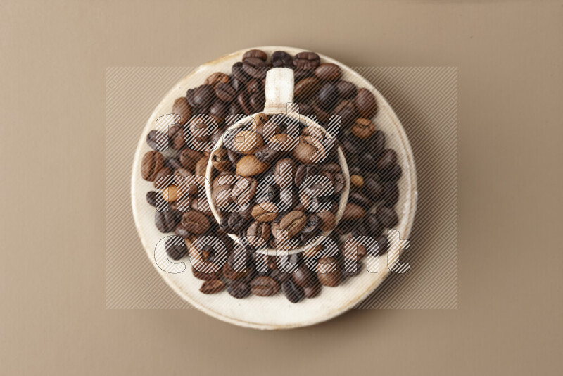 A beige pottery cup full of roasted coffee beans on beige background