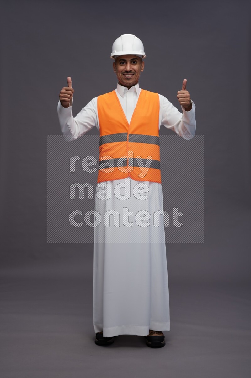 Saudi man wearing thob with engineer vest standing interacting with the camera on gray background