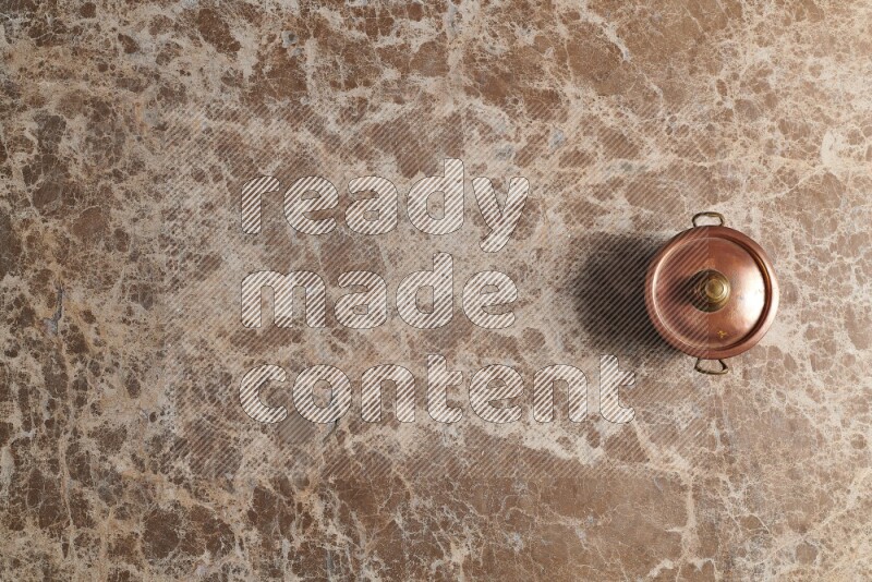 A small copper pot on beige marble background