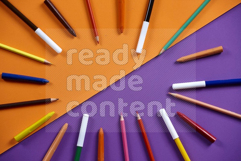 A mix of colored pencils, pens, crayons on orange and purple background (kids toys)