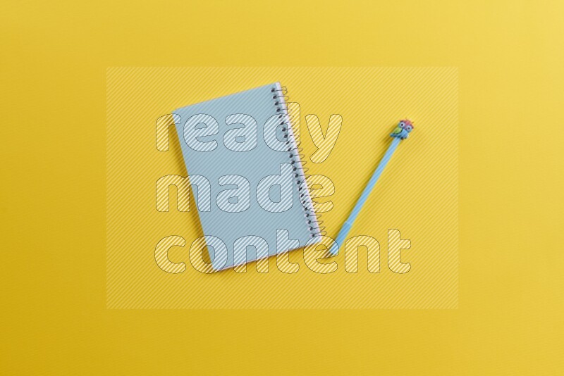 A blue notebook with different school supplies on yellow background