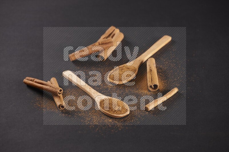 Cinnamon powder in two wooden spoons with cinnamon sticks on black background