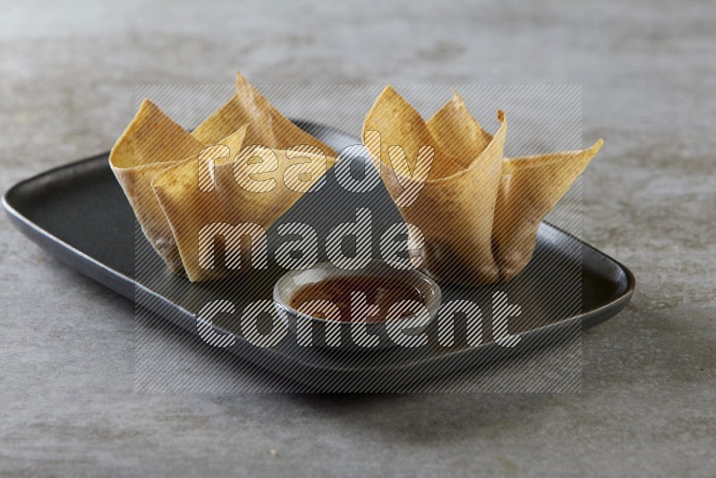 wonton cups with soy sauce ramkin on rectangle dark grey ceramic plate on grey textured counter top