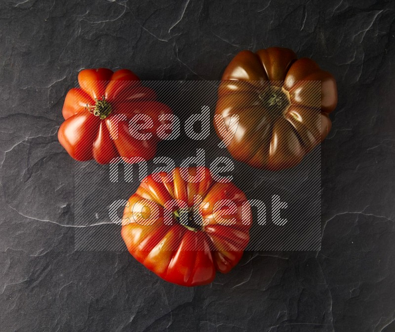 three heirloom tomatoes topview on a black slate background