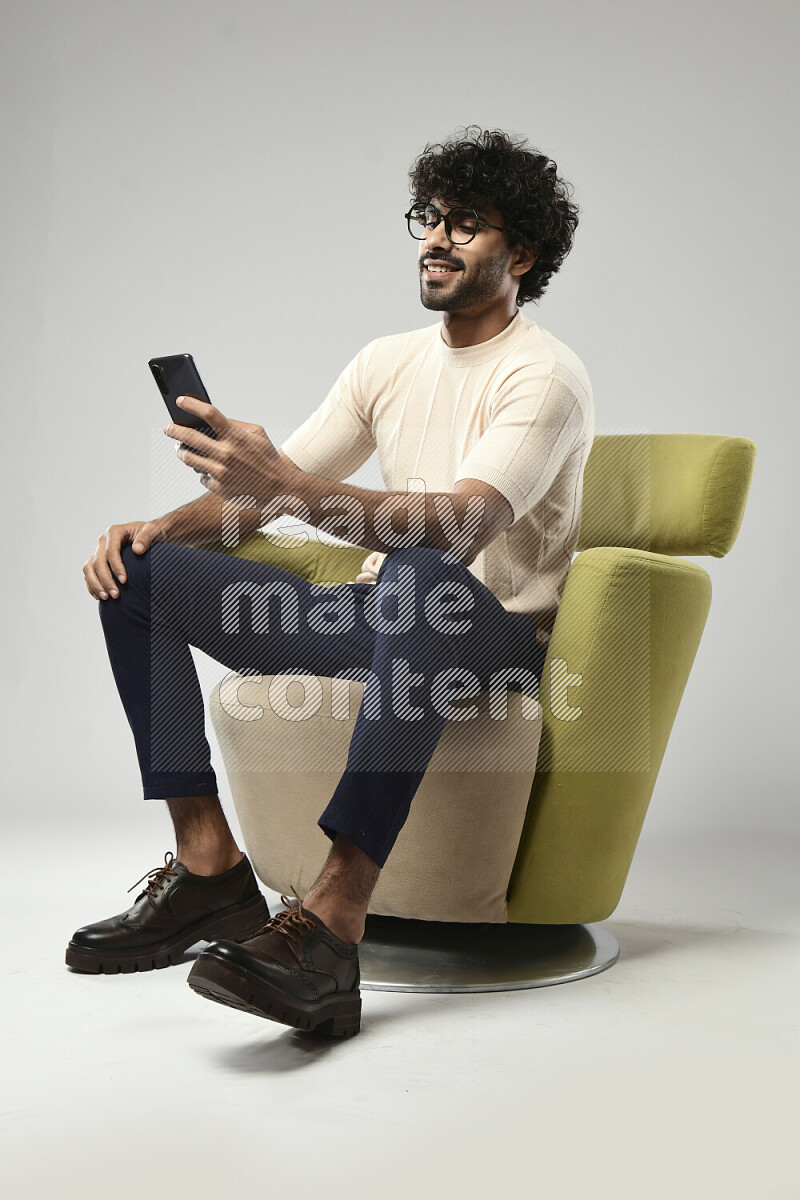 رجل يرتدي ملابس كاجوال يجلس علي كرسي و يتصفح الهاتف علي خلفية بيضاء