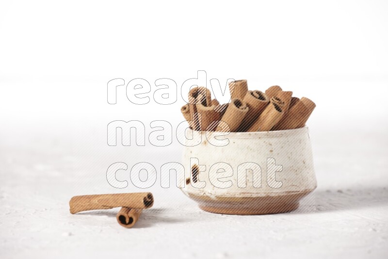 Cinnamon sticks in a beige bowl on a white background