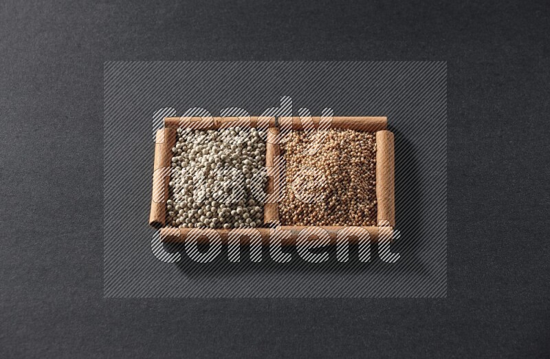 مربعان من أعواد القرفة ممتلئان بحبوب الخردل وحبوب الفلفل الأبيض علي خلفية سوداء