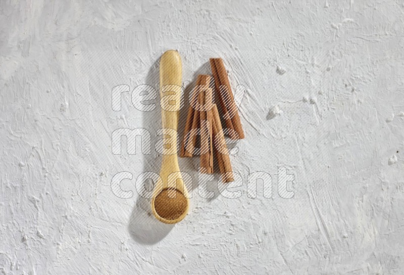Cinnamon powder in a wooden spoon with cinnamon sticks on white background