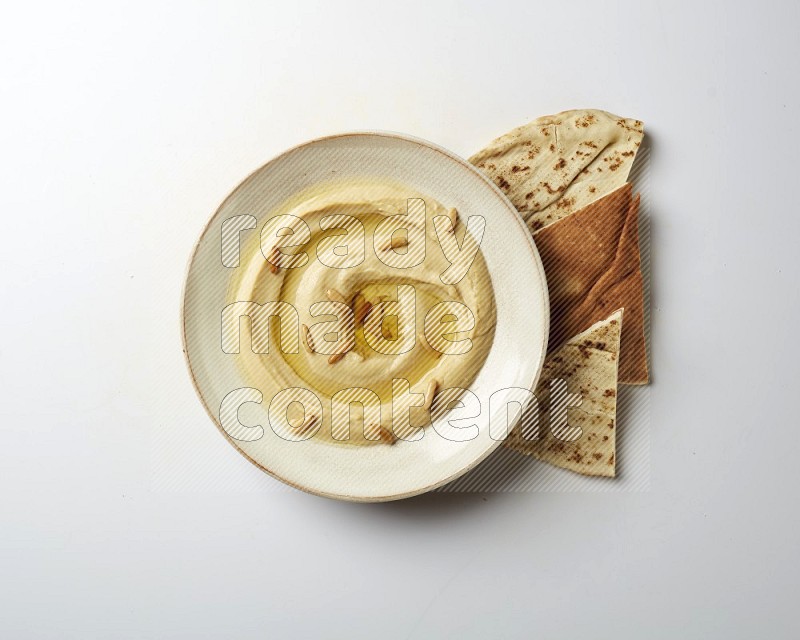Hummus in a pottry plate garnished with pine nuts on a white background