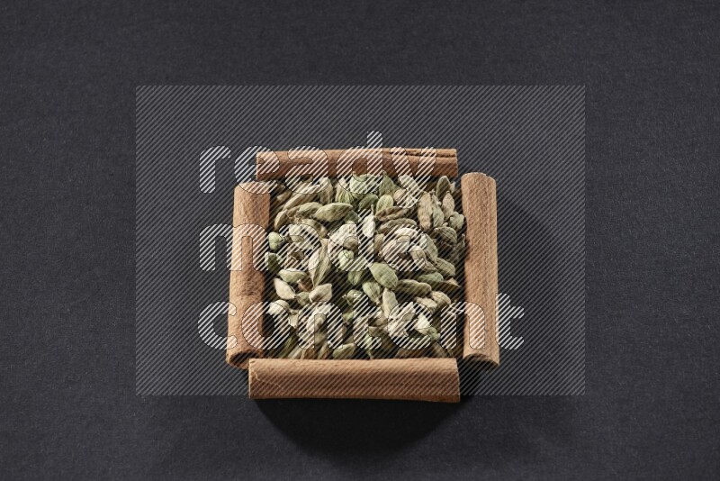 A single square of cinnamon sticks full of Cardamom on black flooring