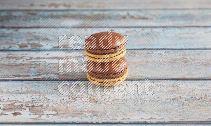 45º Shot of two Yellow and Brown Chai Latte macarons on light blue wooden background
