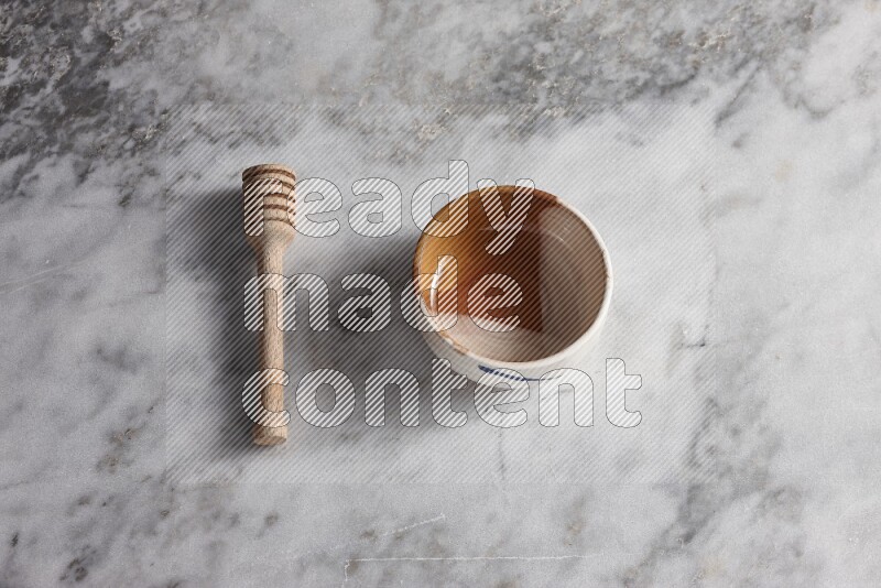 Multicolored pottery bowl with wooden honey dipper on the side on grey marble background
