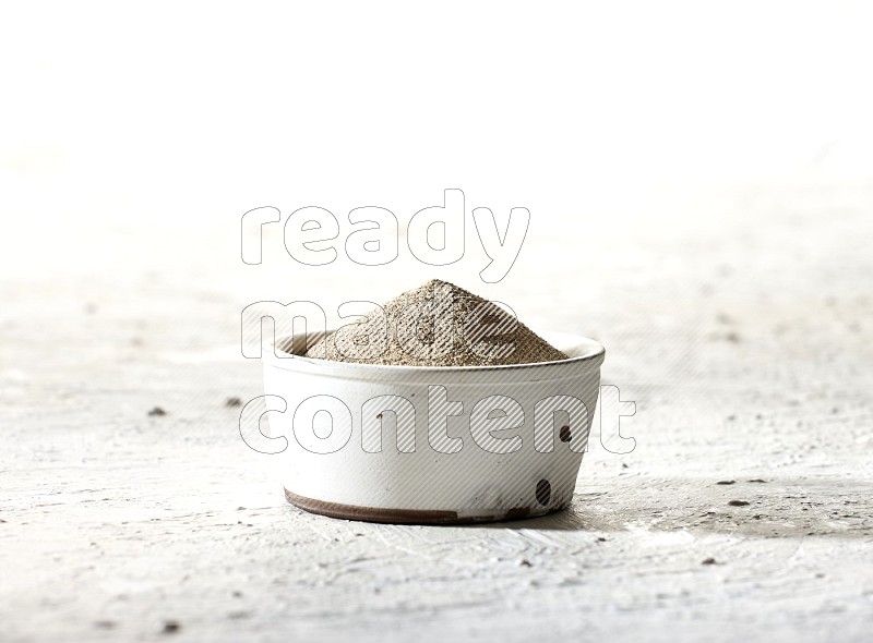 white pottery bowl full of white pepper powder on textured white flooring
