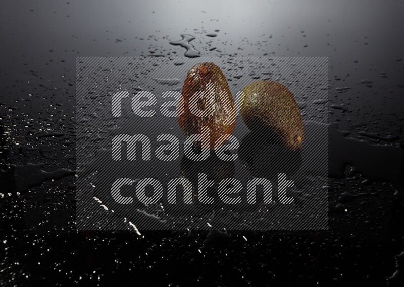 A whole avocado on black background with water drops.