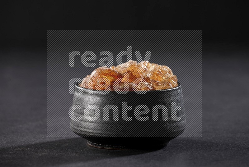 A black pottery bowl full of gum arabic on black flooring in different angles