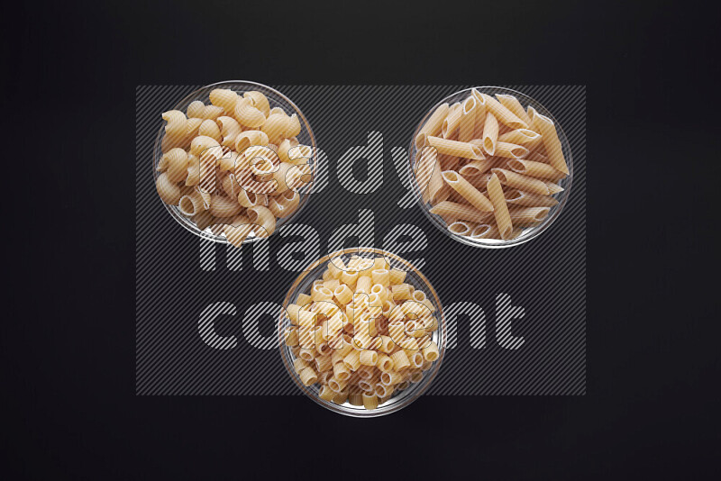 Different pasta types in glass bowls on black background