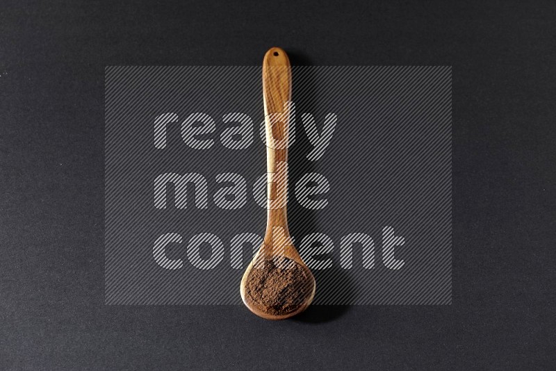 A wooden ladle full of cloves powder on a black flooring