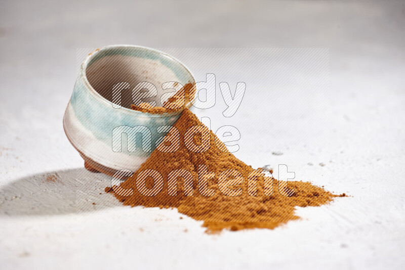 A colored pottery bowl full of ground paprika powder with fallen powder from it on white background