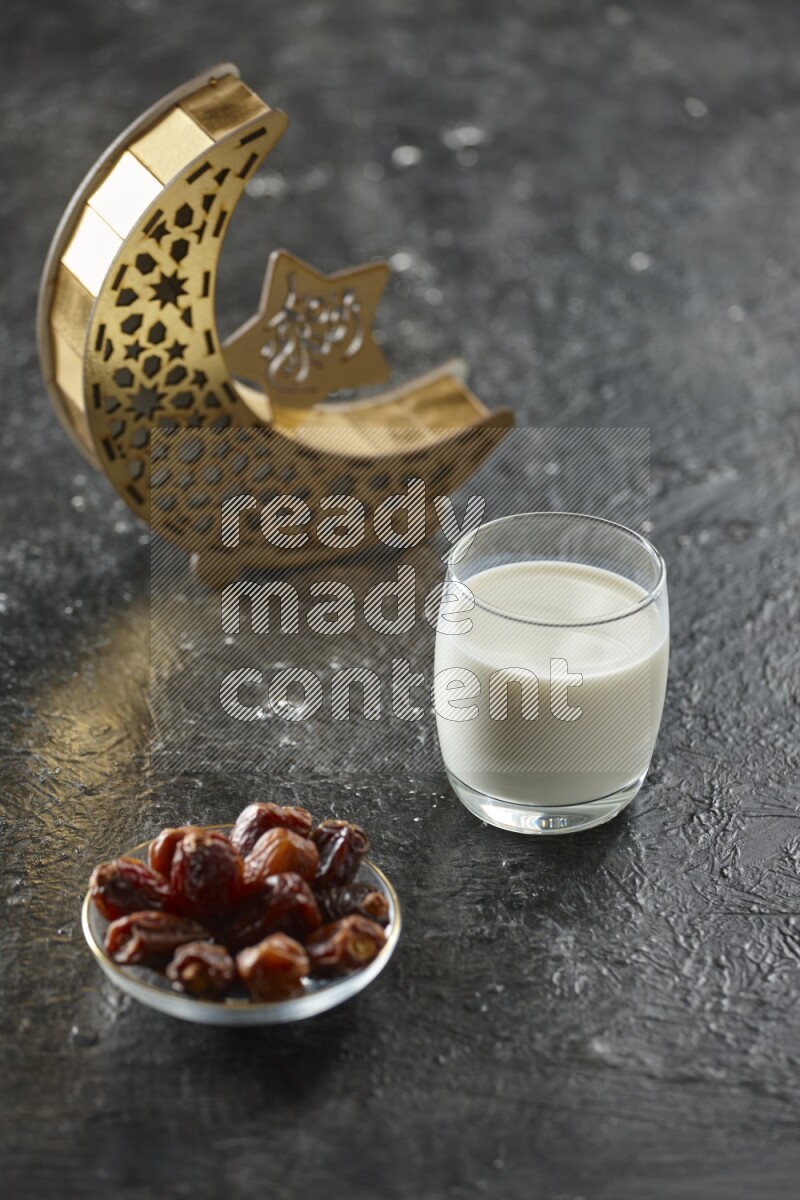 A wooden golden crescent lantern with different drinks, dates, nuts, prayer beads and quran on textured black background