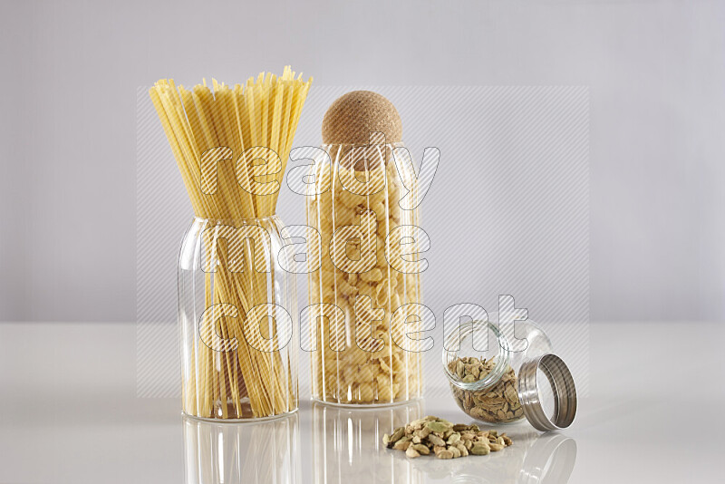 Raw pasta in glass jars with cardamom on light grey background
