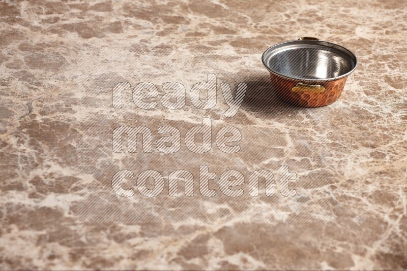 A small copper pot on beige marble background
