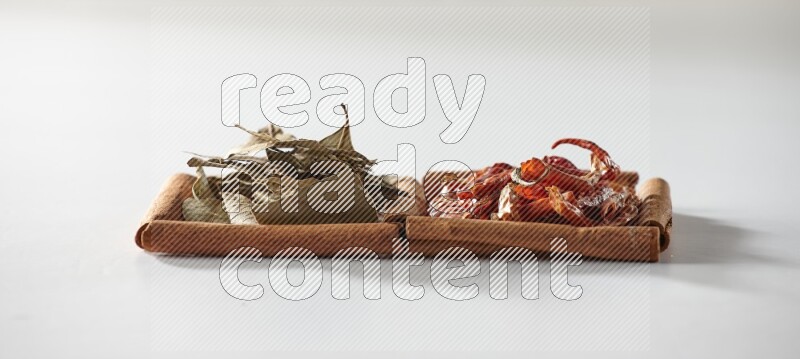 مربعان من أعواد القرفة ممتلئان بالفلفل الحار المجفف وأوراق الغار علي خلفية بيضاء