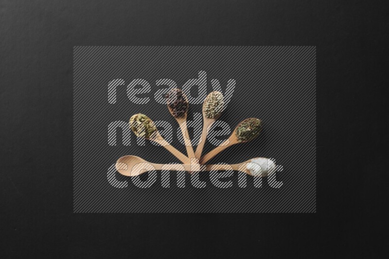 الفلفل الأبيض والقرنفل والهيل والملح والفلفل الأسود وريحان مجفف في معالق خشبية علي خلفية سوداء